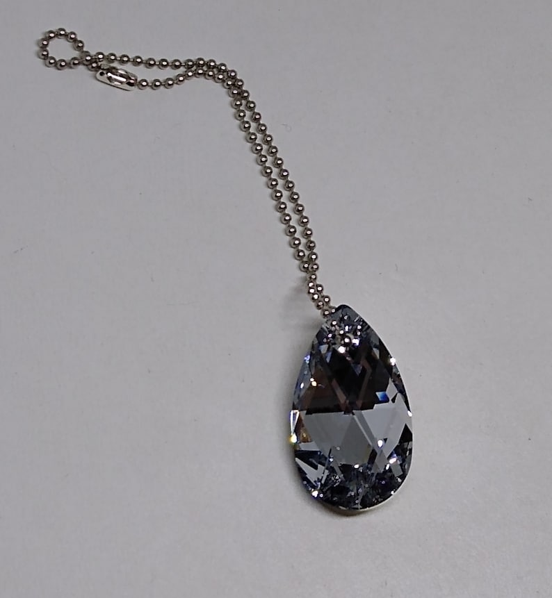 May include: A silver chain necklace with a teardrop-shaped crystal pendant. The crystal is clear with a slight blue tint.
