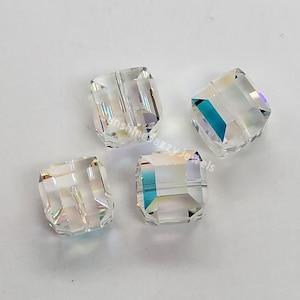 May include: Four clear glass square beads with a hole through the center. The beads have a rainbow iridescent effect.