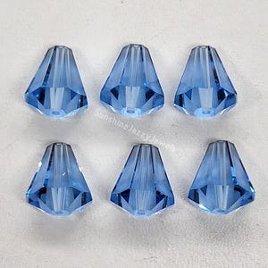 Puede incluir: Seis cuentas de cristal azul claro con un diseño puntiagudo y facetado. Las cuentas están dispuestas en dos filas de tres.