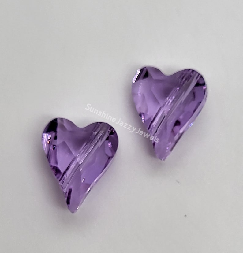 K&ouml;nnte beinhalten: Zwei violette herzf&ouml;rmige Glasperlen mit facettiertem Design.