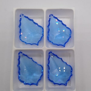 May include: Four light blue crystal teardrop shaped pendants with a blue iridescent finish, displayed in a white plastic tray.