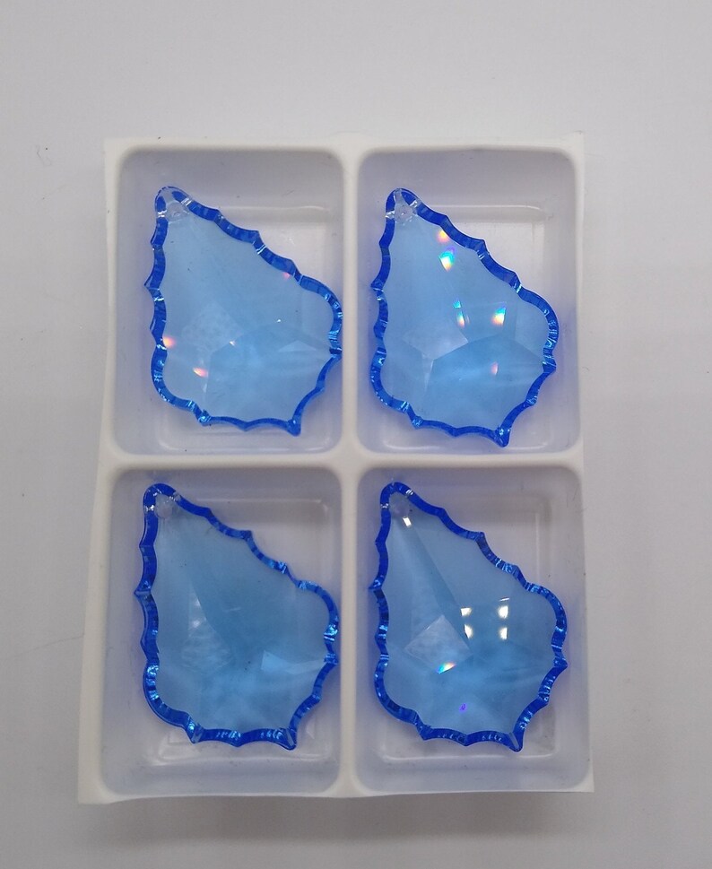 May include: Four light blue crystal teardrop shaped pendants with a blue iridescent finish, displayed in a white plastic tray.