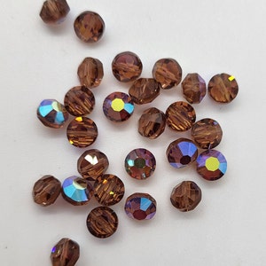 May include: A collection of brown iridescent glass beads. The beads are round and have a faceted design.