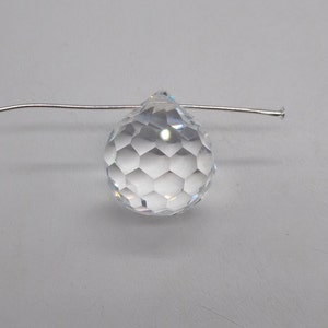 May include: A clear crystal teardrop prism with a faceted design, hanging from a silver wire.
