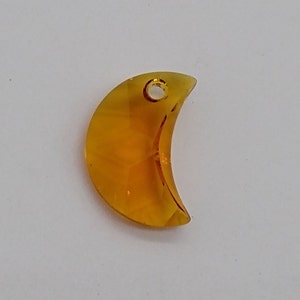 May include: A crescent moon-shaped glass charm in a translucent amber color with a small hole at the top for hanging.