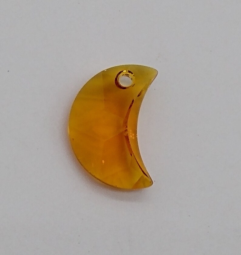 May include: A crescent moon-shaped glass charm in a translucent amber color with a small hole at the top for hanging.