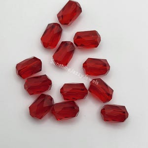 May include: A group of 12 red faceted glass beads. The beads are rectangular in shape and have a shiny finish.