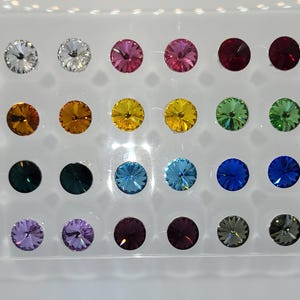May include: Assortment of 20 round, flat-backed rhinestones in various colors, including clear, pink, red, yellow, green, blue, and purple. The rhinestones are arranged in a grid pattern on a white background.