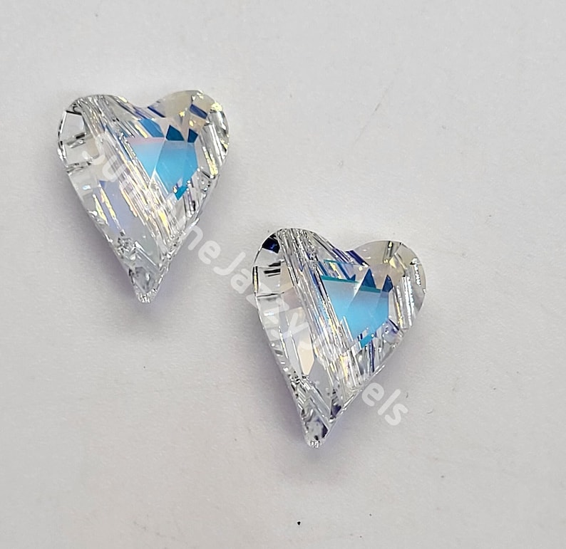 May include: Two clear crystal heart-shaped charms with a faceted design. The charms have a rainbow iridescent effect.