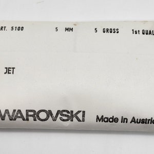 May include: A white package with black text that reads "ART. 5100 5 MM 5 GROSS 1st QUALITY JET SWAROVSKI Made in Austria".