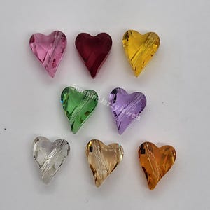 K&ouml;nnte beinhalten: Acht herzf&ouml;rmige Kristallperlen in verschiedenen Farben, darunter rosa, rot, gelb, gr&uuml;n, lila, klar, hellbraun und orange.