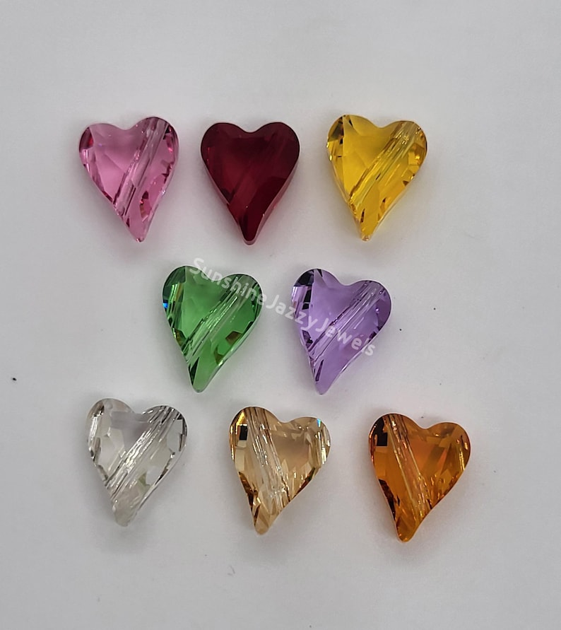 K&ouml;nnte beinhalten: Acht herzf&ouml;rmige Kristallperlen in verschiedenen Farben, darunter rosa, rot, gelb, gr&uuml;n, lila, klar, hellbraun und orange.