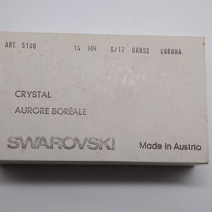 K&ouml;nnte beinhalten: Eine wei&szlig;e Box mit dem Text "ART. 5100 14 MM 6/12 GROSS CORONA" und "CRYSTAL AURORE BOR&Eacute;ALE SWAROVSKI Made in Austria".