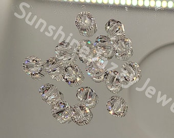 May include: A group of clear crystal beads with a faceted design. The beads are arranged in a cluster on a reflective surface.