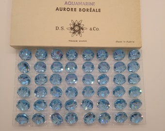 Puede incluir: Primer plano de un paquete de cuentas de aguamarina aurora boreal de 12 mm. El paquete está etiquetado con "4/12 gross 12 mm", "Art. 335 5100", "AQUAMARINE AURORE BORÉALE", "D.S. & Co.", "TRADE MARK" y "Made in Austria".