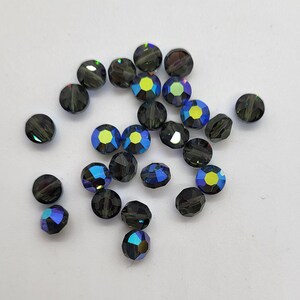 May include: A scattering of dark blue iridescent glass beads, some with a hint of green, on a white background.