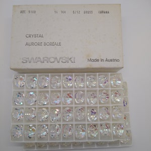 K&ouml;nnte beinhalten: Eine Schachtel mit 14 mm gro&szlig;en, klaren Kristallperlen mit irisierendem Finish. Die Schachtel ist mit "Swarovski" und "Made in Austria" beschriftet.