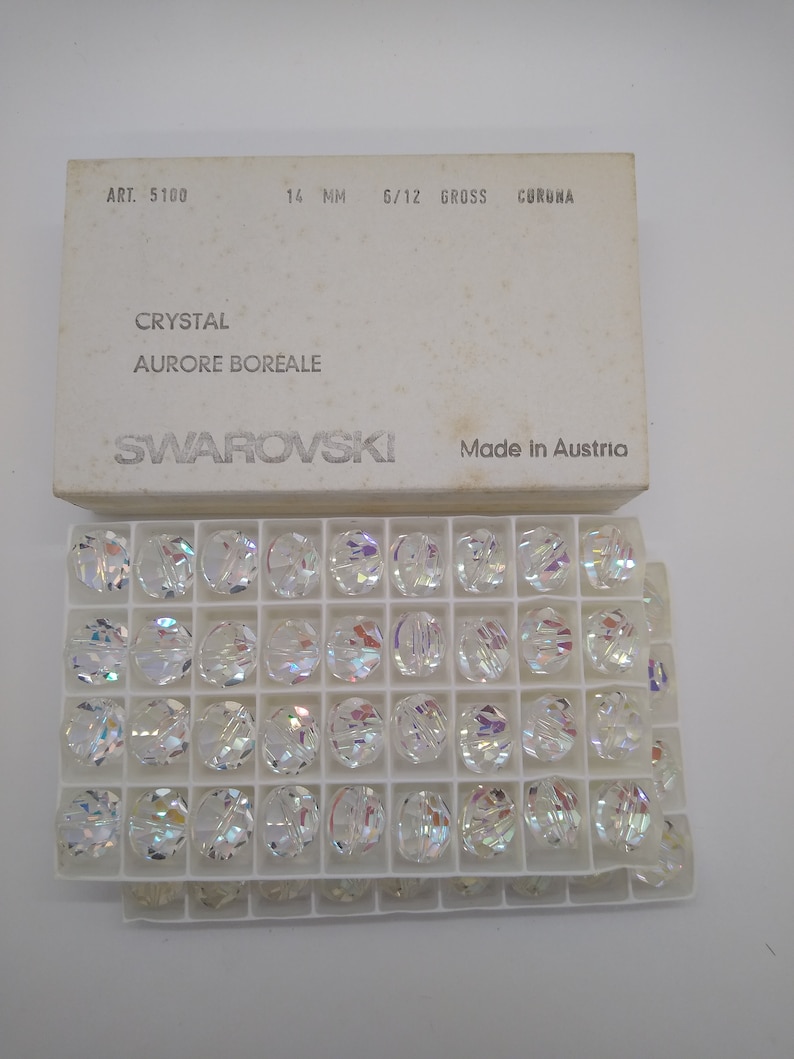 K&ouml;nnte beinhalten: Eine Schachtel mit 14 mm gro&szlig;en, klaren Kristallperlen mit irisierendem Finish. Die Schachtel ist mit "Swarovski" und "Made in Austria" beschriftet.