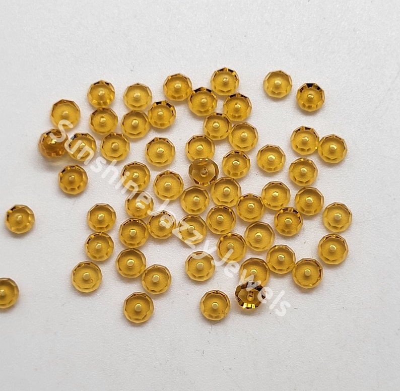 May include: A collection of small, round, faceted, amber-colored glass beads. The beads are scattered on a white surface.