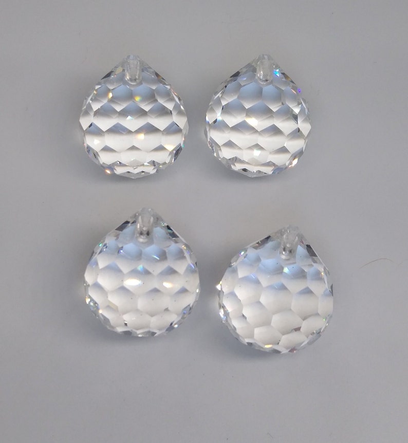 May include: Four clear crystal faceted teardrop shaped pendants with a hole at the top for hanging.