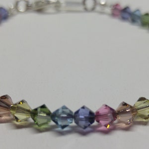 May include: A rainbow crystal bracelet with a silver clasp. The bracelet is made of small, faceted crystals in shades of pink, blue, green, and yellow.