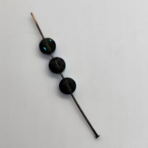 May include: Three black beads with iridescent accents are strung on a thin wire.