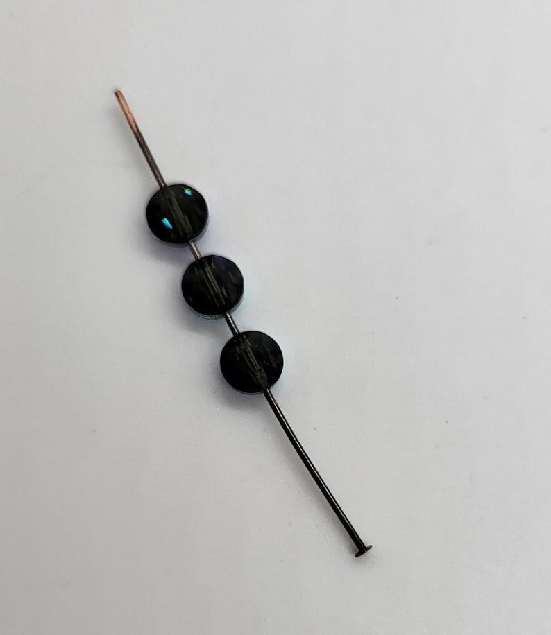May include: Three black beads with iridescent accents are strung on a thin wire.