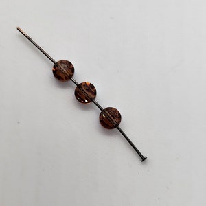 May include: Three brown glass beads strung on a thin black wire.