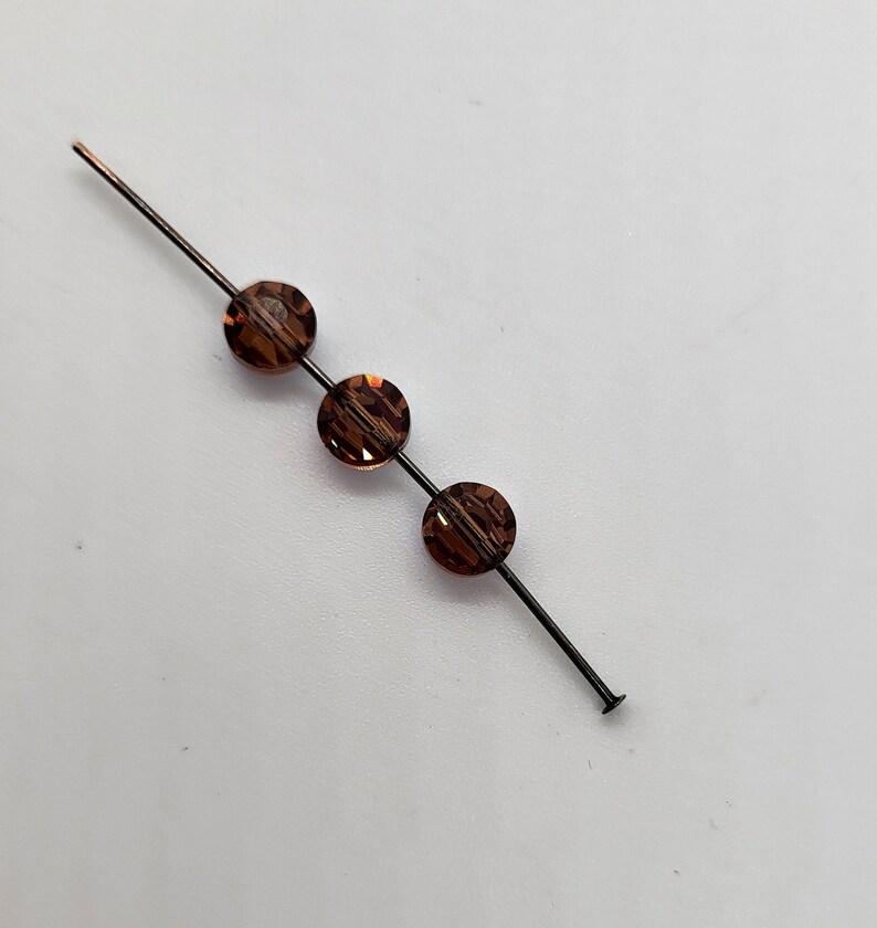 May include: Three brown glass beads strung on a thin black wire.
