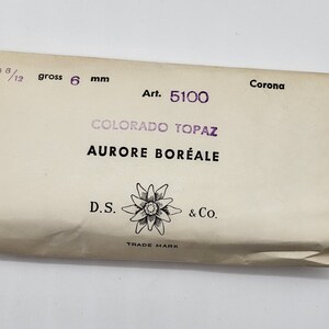 May include: A white paper package with the text "Corona Art. 5100 COLORADO TOPAZ AURORE BOR&Eacute;ALE D.S. & Co. TRADE MARK" printed on it. The package is labeled with "2 6/12 gross 6 mm".