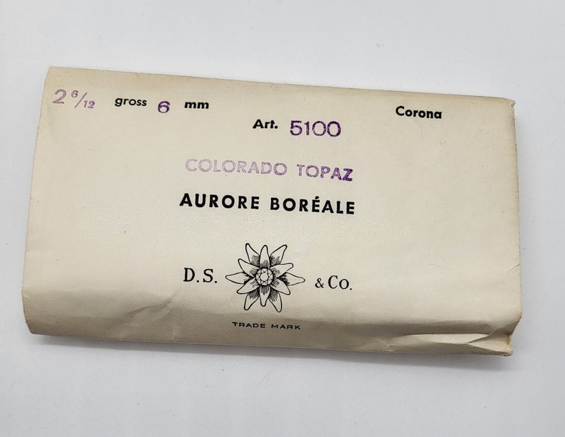 May include: A white paper package with the text "Corona Art. 5100 COLORADO TOPAZ AURORE BOR&Eacute;ALE D.S. & Co. TRADE MARK" printed on it. The package is labeled with "2 6/12 gross 6 mm".