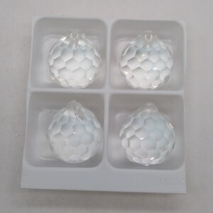 May include: Four clear glass crystal balls with a faceted design, packaged in a white plastic tray.