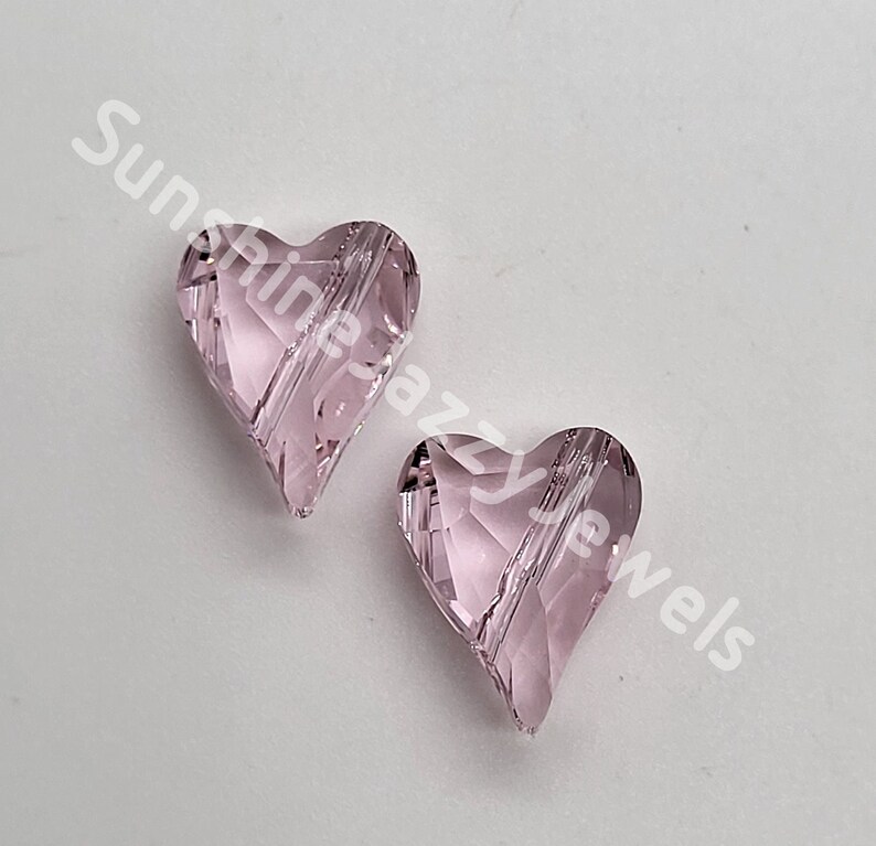 May include: Two pink glass heart-shaped beads with a faceted design. The beads are approximately 1 inch in size.