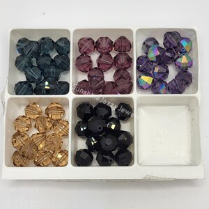 May include: A white plastic organizer filled with faceted beads in various colors. The beads are in shades of blue, purple, gold, and black. The beads are round and have multiple facets.