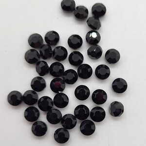 May include: A collection of black round rhinestones, scattered on a white surface.