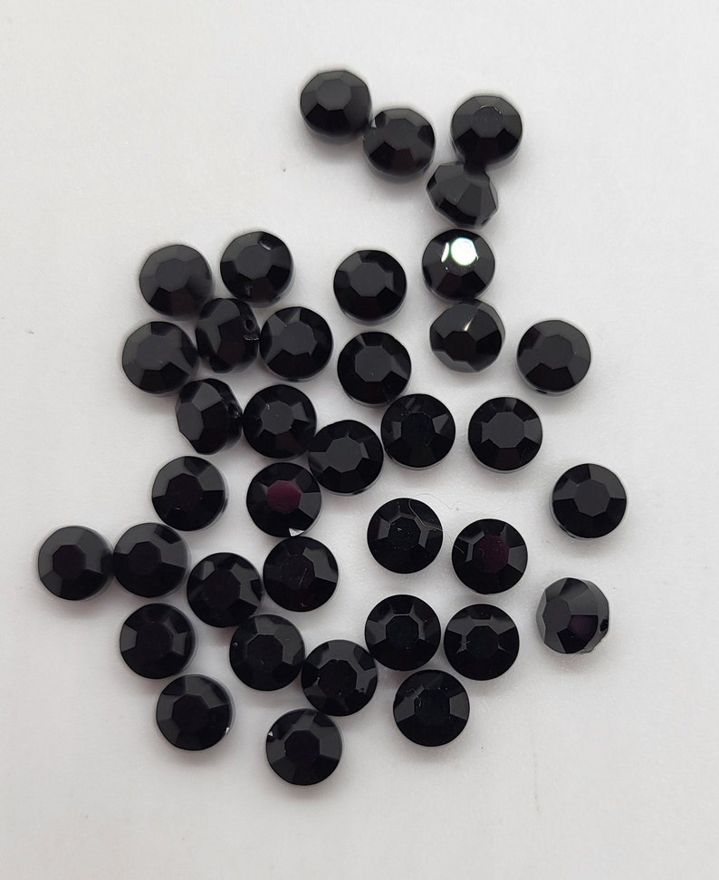 May include: A collection of black round rhinestones, scattered on a white surface.