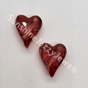 May include: Two red heart-shaped glass beads with a striated pattern. The beads are on a white background.