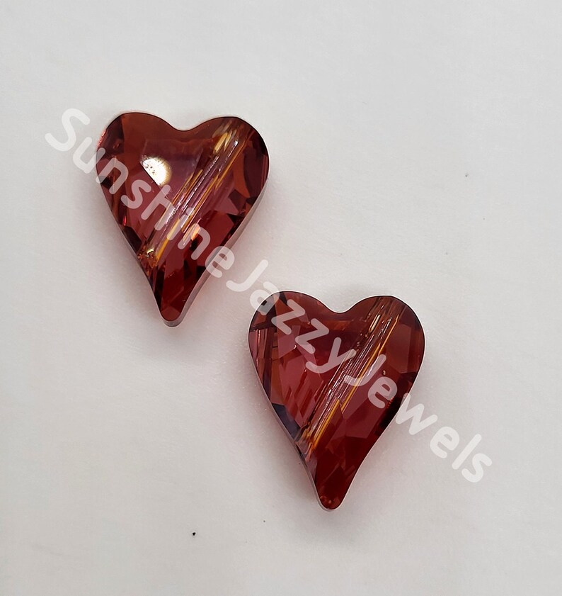May include: Two red heart-shaped glass beads with a striated pattern. The beads are on a white background.