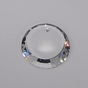 May include: A clear crystal prism with a round shape and a hole at the top for hanging. The prism has a faceted design that creates rainbow reflections.