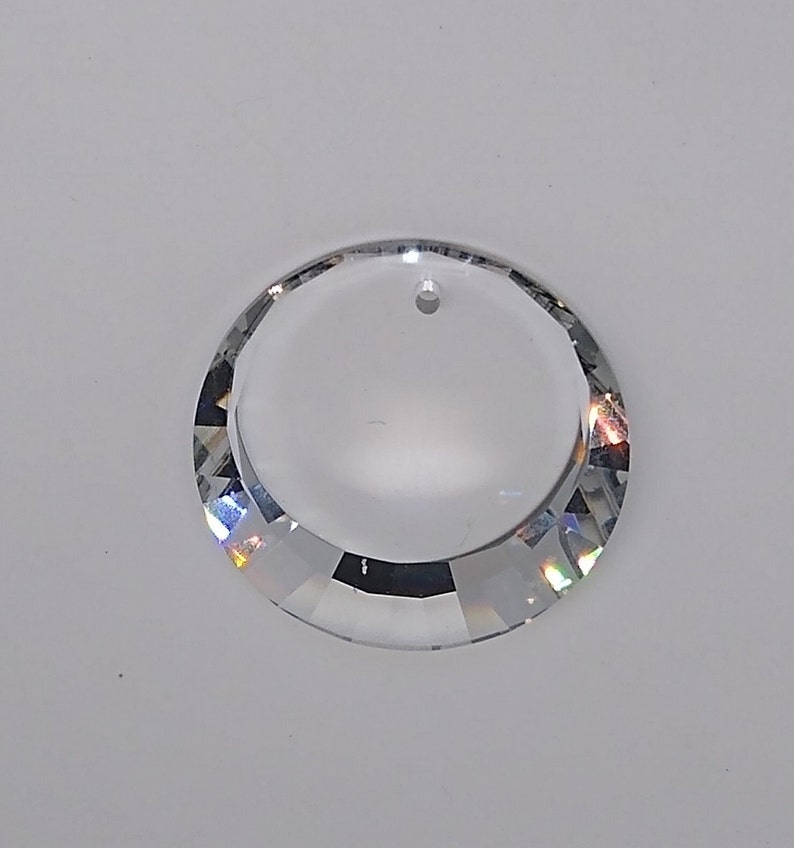 May include: A clear crystal prism with a round shape and a hole at the top for hanging. The prism has a faceted design that creates rainbow reflections.