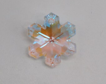 May include: A clear iridescent snowflake charm with a light pink hue. The charm has a hole at the top for hanging.
