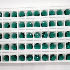 May include: A white tray with 40 emerald green glass beads arranged in rows. The beads are faceted and have a round shape.