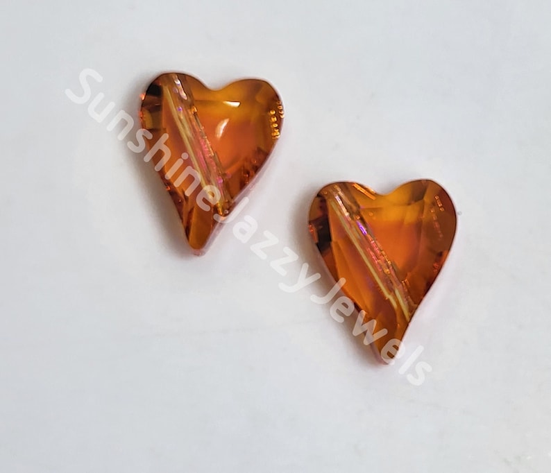 May include: Two amber heart-shaped glass beads with a clear iridescent finish.