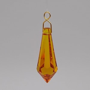 May include: A teardrop-shaped amber crystal prism with a gold-colored metal loop at the top.