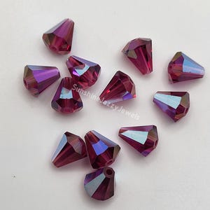 May include: A group of 12 purple iridescent glass teardrop beads. The beads are faceted and have a pointed tip. They are perfect for jewelry making.