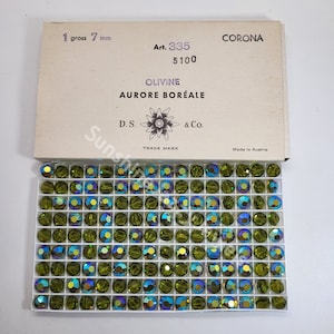 K&ouml;nnte beinhalten: Eine Schachtel mit 7 mm gro&szlig;en gr&uuml;nen Glasperlen mit einem Etikett mit der Aufschrift "CORONA Art. 335 5100 OLIVINE AURORE BOR&Eacute;ALE D.S. & Co. TRADE MARK Made in Austria".