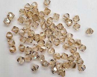 May include: A scattering of small, gold-toned glass beads with a faceted, pyramid-like shape. The beads have a subtle iridescent shimmer.