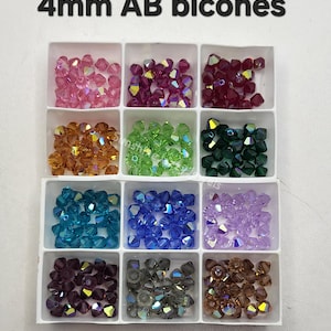 May include: A white divided tray filled with 4mm AB bicone beads in various colors. The colors include pink, purple, red, orange, green, dark green, teal, blue, lavender, dark purple, gray, and brown. The text "4mm AB bicones" is at the top.