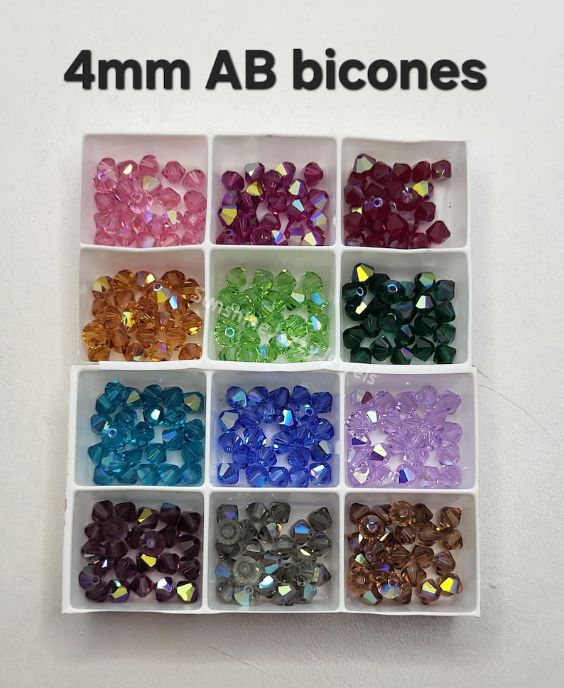 May include: A white divided tray filled with 4mm AB bicone beads in various colors. The colors include pink, purple, red, orange, green, dark green, teal, blue, lavender, dark purple, gray, and brown. The text "4mm AB bicones" is at the top.