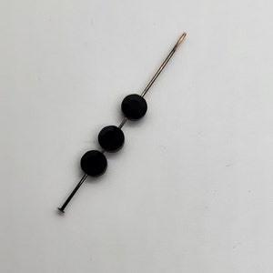 May include: Three black round beads threaded onto a silver wire.